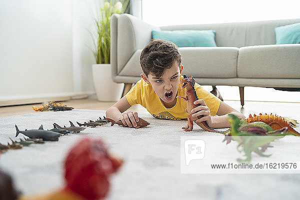 Junge schreit beim Spielen mit Spielzeugtieren auf dem Teppich im Wohnzimmer