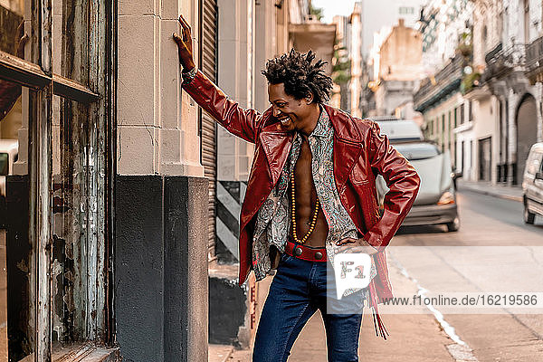 Happy retro man wearing leather jacket while standing on sidewalk during sunny day