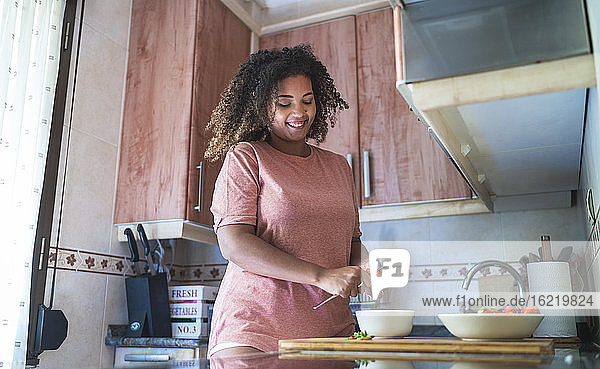 Lächelnde junge Frau beim Schneiden von Erdbeeren auf dem Küchentisch zu Hause