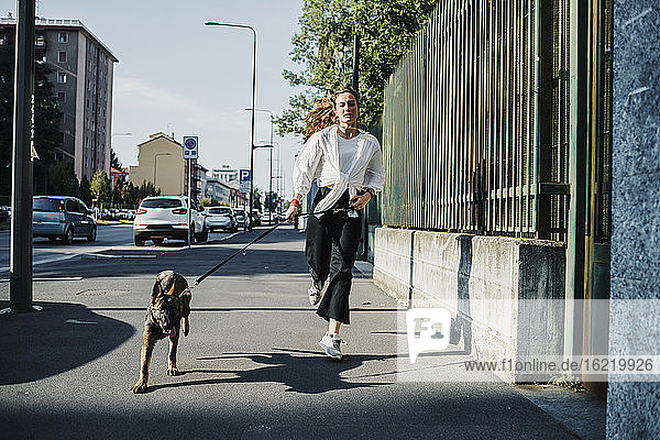 Frau läuft mit Hund auf dem Bürgersteig in der Stadt