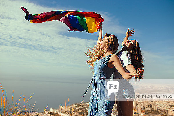 Two cheerful young women with an LGBT flag above the coastal city of Almeria  Spain