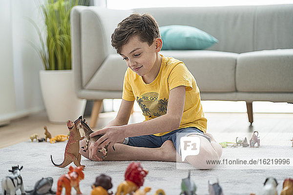 Lächelnder Junge spielt mit Spielzeugtieren im Wohnzimmer zu Hause