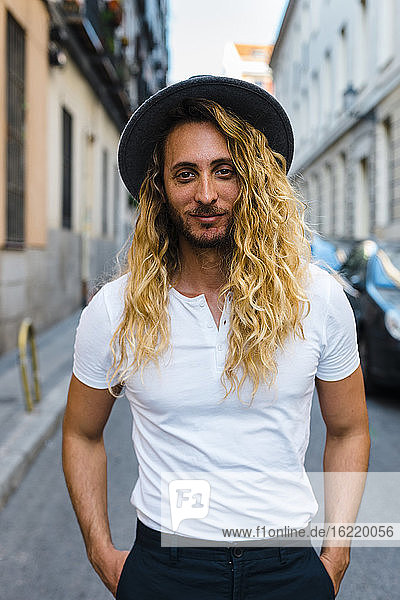Stylish mid adult man with long hair wearing hat while standing on street in city