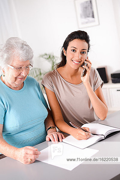 cheerful young woman helping an old senior person doing paperwork and telephone call