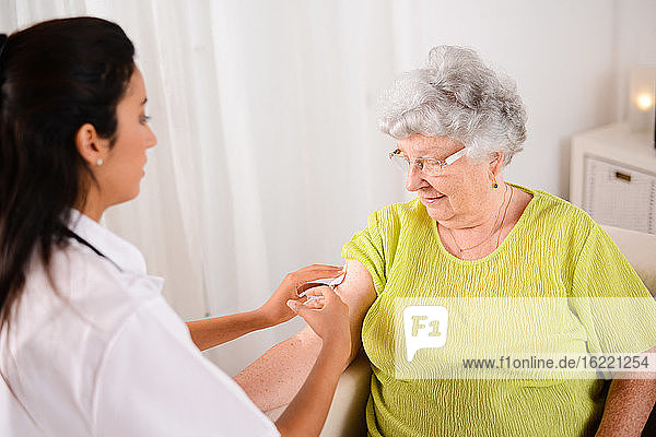 cheerful young nurse giving an injection to a elderly senior woman at home