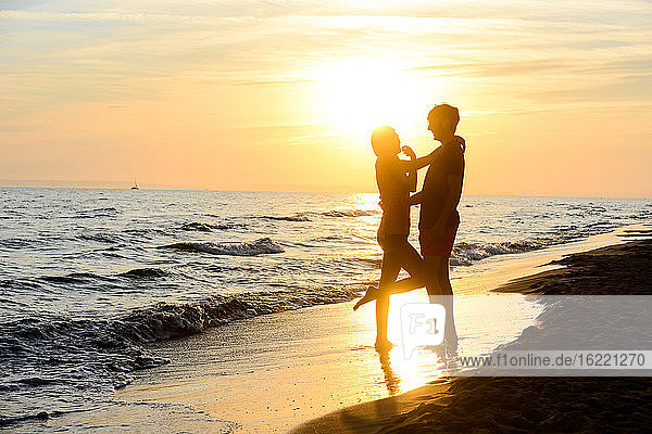 romantic young couple in love together in the sand along the beach of mediterranean sea sunset backlight