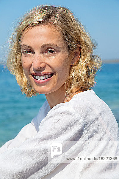 Porträt einer hübschen lächelnden blonden Frau vor dem Meer.