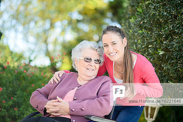 Fröhliche junge Frau im Garten eines Seniorenheims mit einer älteren Dame.