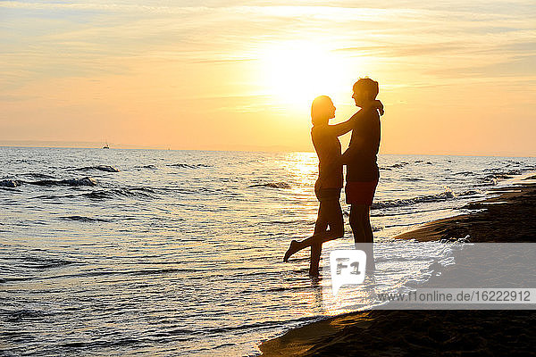 romantic young couple in love together in the sand along the beach of mediterranean sea sunset backlight