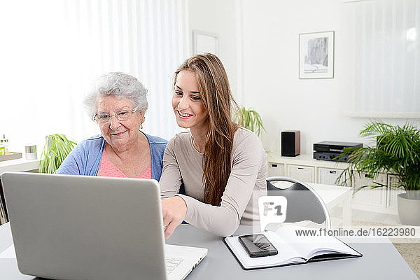 Young woman helping old senior woman doing paperwork and administrative procedures with laptop computer at home