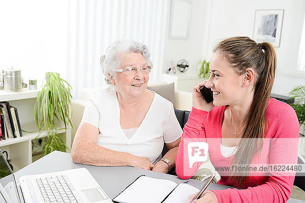 Junge Frau hilft einer älteren Frau bei der Erledigung von Papierkram und Verwaltungsaufgaben mit einem Laptop zu Hause