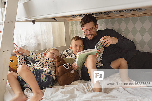 Vater mit Söhnen  die auf dem Bett ein Buch lesen