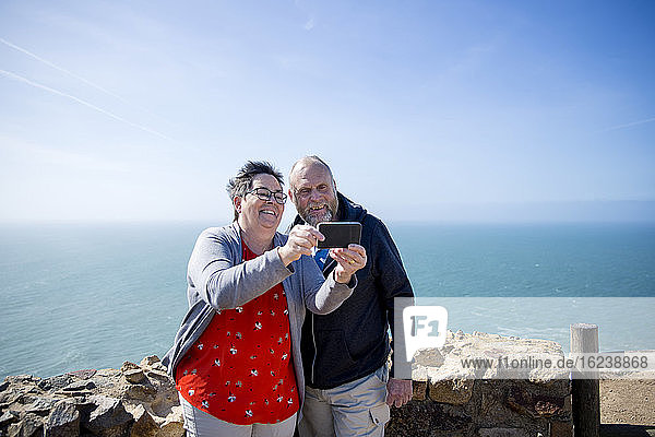 Lächelndes Paar nimmt Selfie  Meer im Hintergrund
