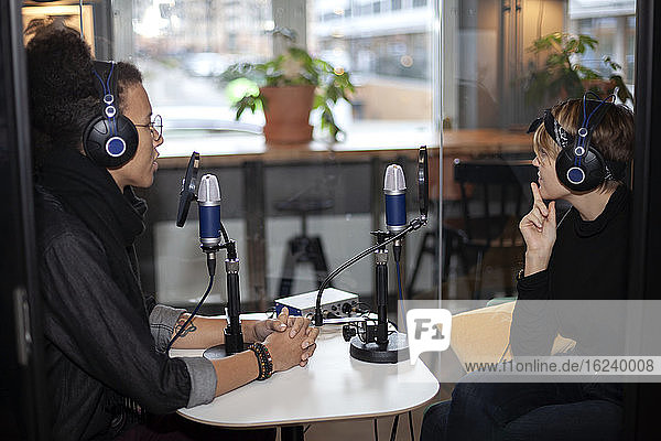 People wearing headphones and sitting at table with microphone