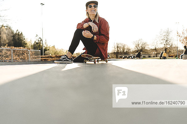 Smiling woman sitting with her skateboard on front