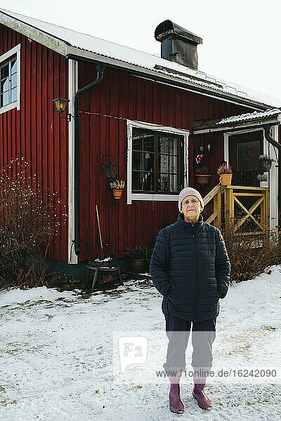 Ältere Frau steht vor einem Holzhaus