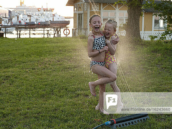 Girls playing with water sprinkler in garden