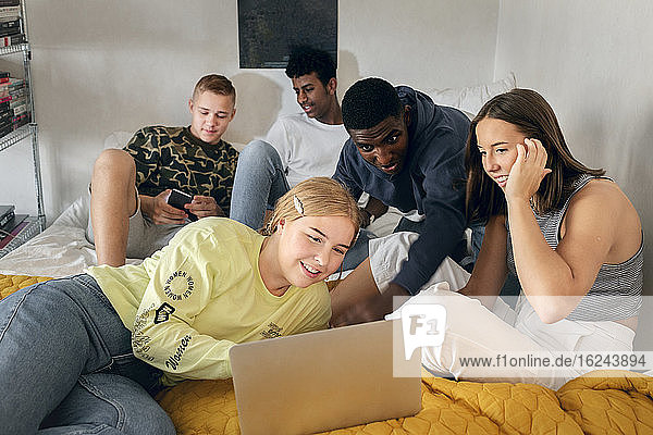 Friends using laptop on bed