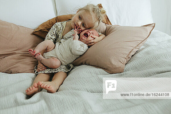 Mädchen mit neugeborenem Geschwisterchen auf dem Bett