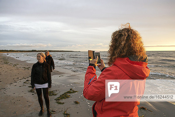 Frau fotografiert Freunde am Strand mit ihrem Smartphone