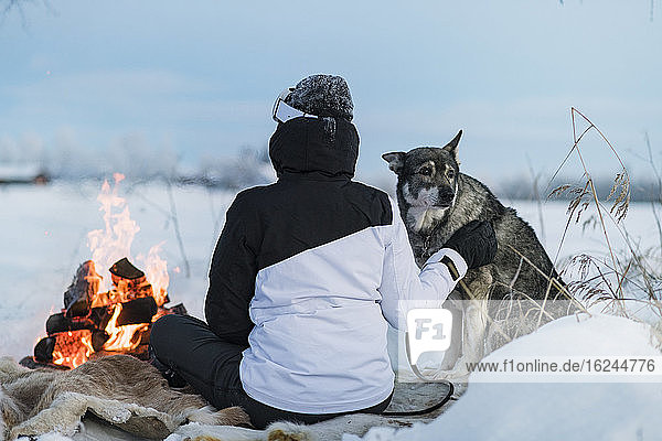 Frau mit Hund sitzt am Lagerfeuer