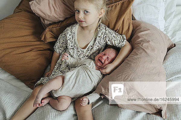 Mädchen mit neugeborenem Geschwisterchen auf dem Bett