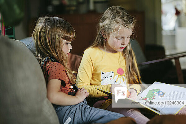 Sisters reading book on sofa
