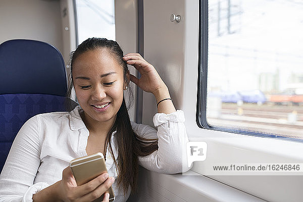 Lächelnde Frau benutzt Handy im Zug