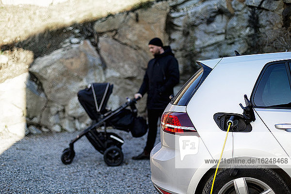 Electric car on charge  man with pram on background