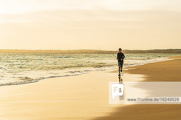 Junge läuft am Strand bei Sonnenuntergang