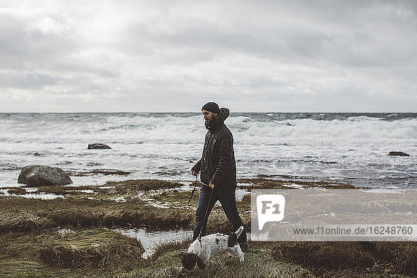 Mann geht mit Hund an der Küste spazieren