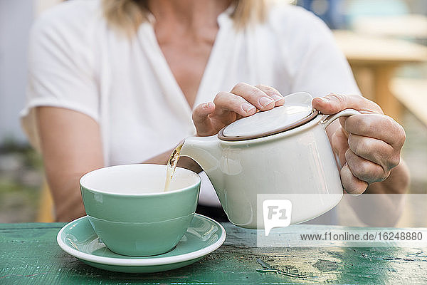 Frau gießt Tee in eine Tasse