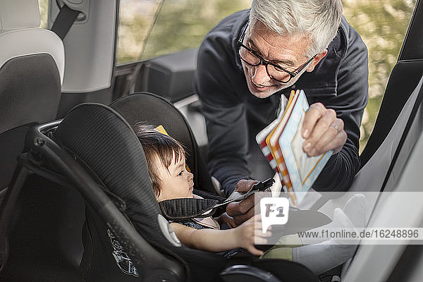 Grandfather fastening baby girl into car safety seat