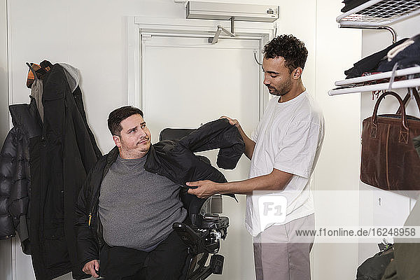 Career helping man in wheelchair putting jacket on