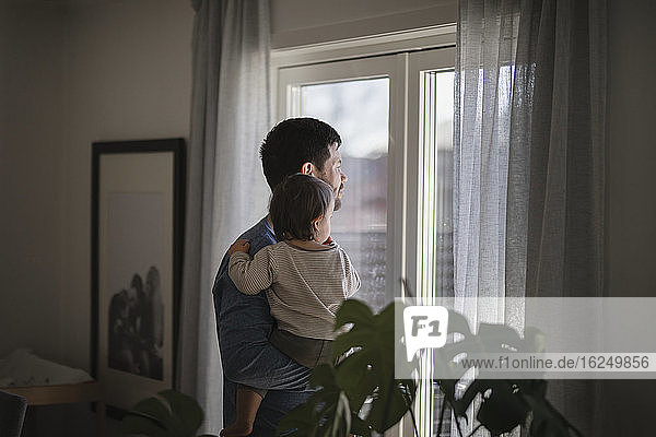 Vater mit Baby schaut durch das Fenster