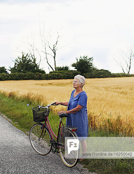 Ältere Frau mit Fahrrad am Feld