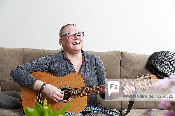 Frau spielt Gitarre auf Sofa
