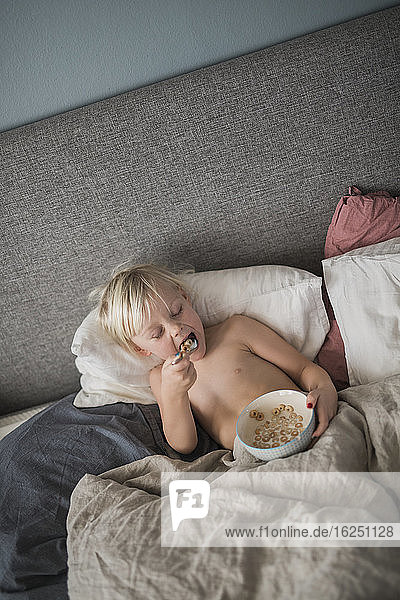 Junge im Bett und isst Müsli