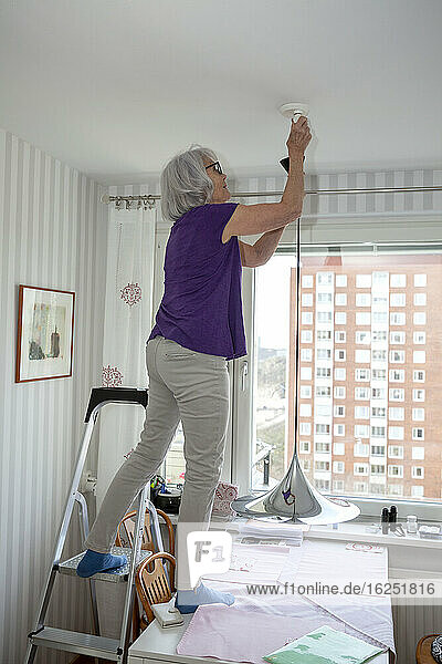Ältere Frau hängt Deckenlampe auf