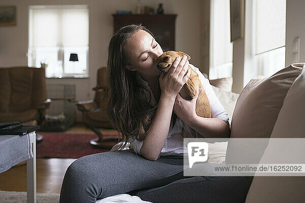 Young woman kissing dog at home