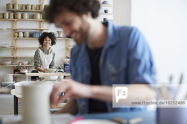 Porträt einer lächelnden Frau  die Töpfern lernt  während ein Mann im Kunstatelier im Vordergrund steht