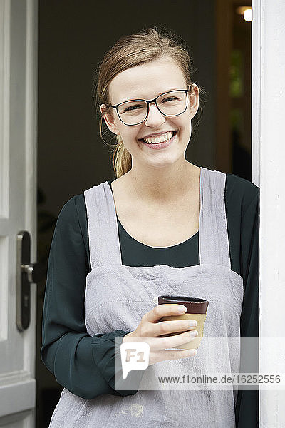Portrait of smiling female owner having coffee at entrance of art studio