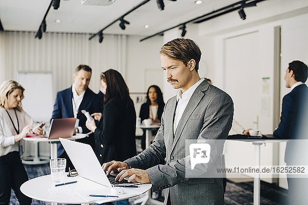 Männlicher Geschäftsmann arbeitet über Laptop  während er im Büro steht Seminar