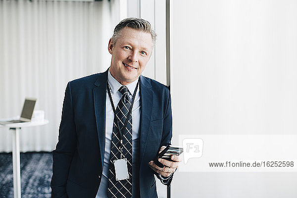 Porträt eines lächelnden Unternehmers mit Mobiltelefon im Büro