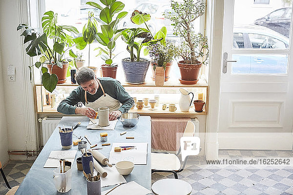 Älterer Mann fertigt Handwerksprodukte bei Tisch in der Töpferklasse