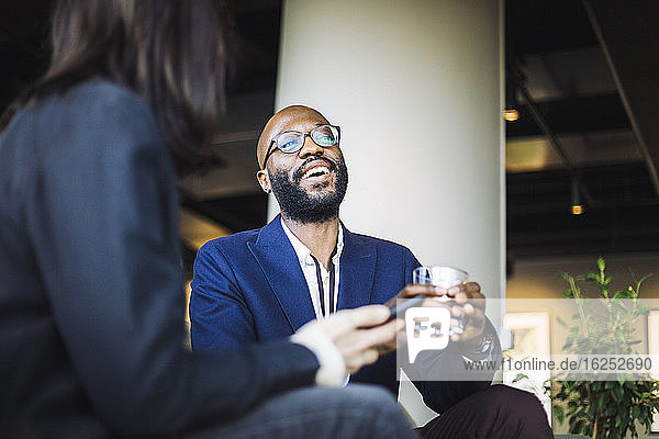 Lächelnder männlicher Unternehmer schaut weg  während er mit einer weiblichen Mitarbeiterin im Büro sitzt