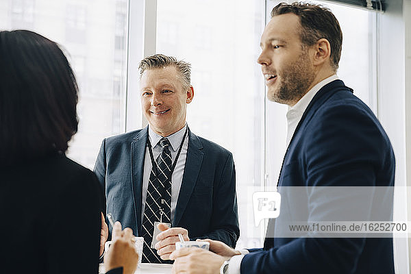 Lächelnde männliche Unternehmer diskutieren mit einer Kollegin im Büroseminar