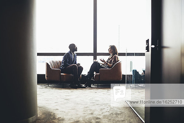 Männliche und weibliche Kollegen diskutieren  während sie am Arbeitsplatz am Fenster sitzen