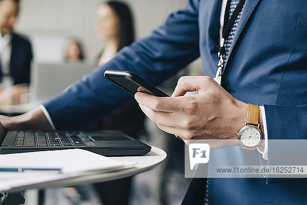 Midsection of businessman using phone while standing in office seminar