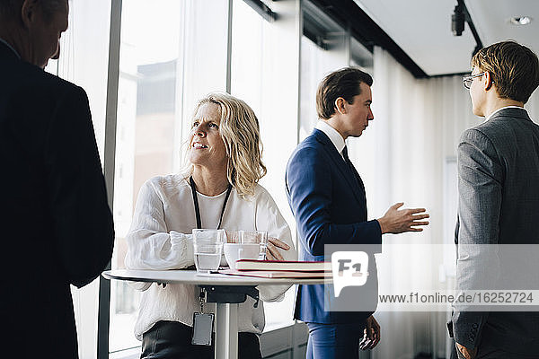 Female entrepreneur talking to colleague while coworker standing in background at workplace